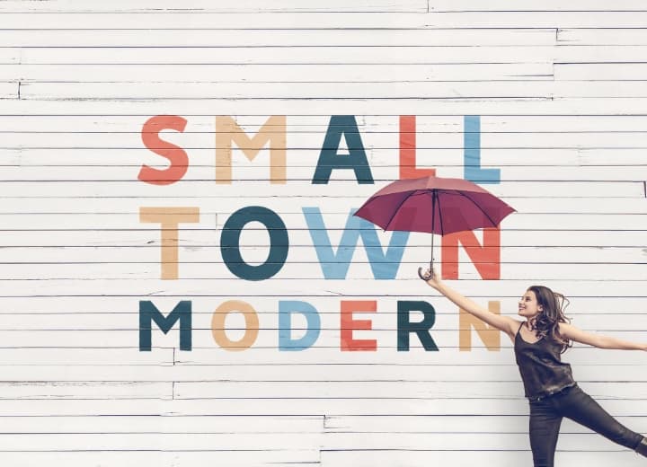 A woman holding an umbrella in front of a white wall with the words small town modern.