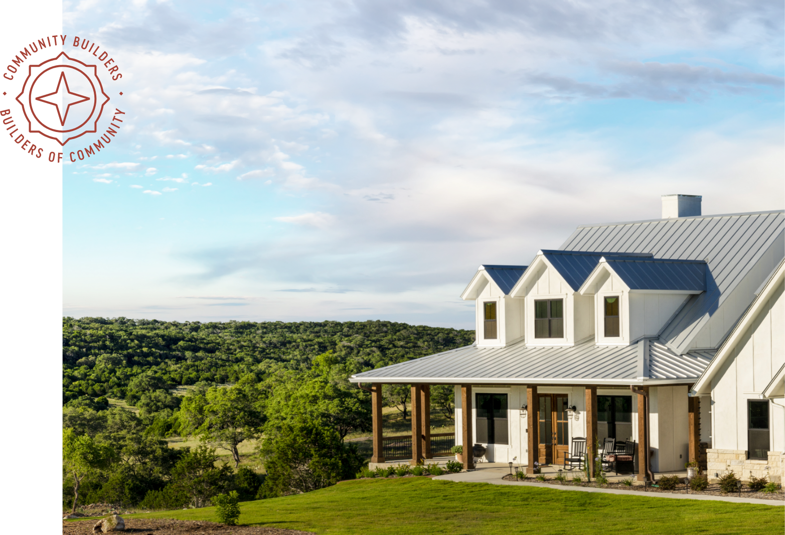 A white farmhouse with a metal roof overlooking a grove of trees