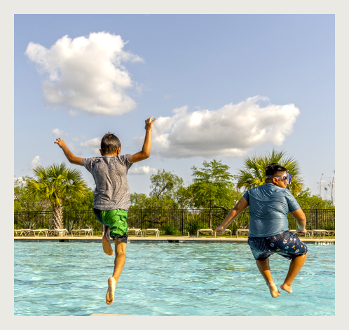 Two boys jumping into a swimming pool.