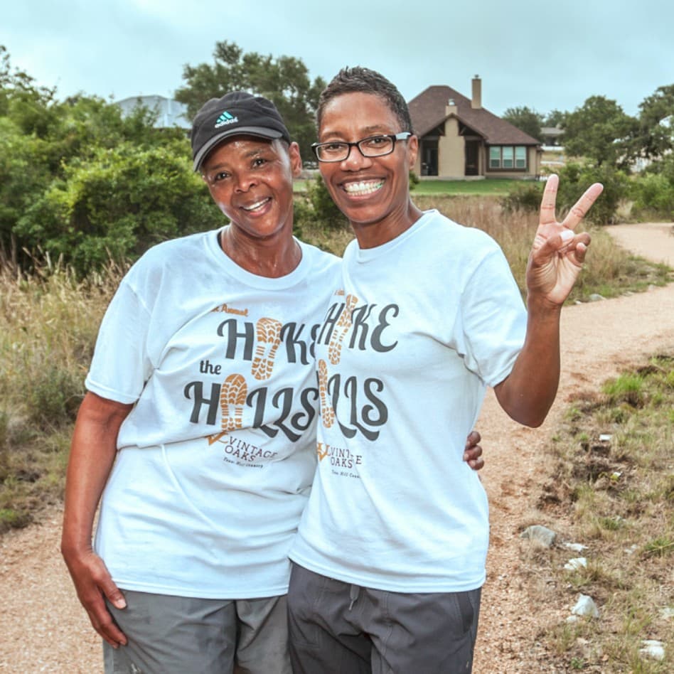 Two women posing for a photo wearing t - shirts while participating in the Hike the Hills charity walk