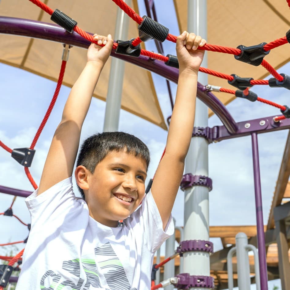 A young boy is climbing on a rope in a playground.
