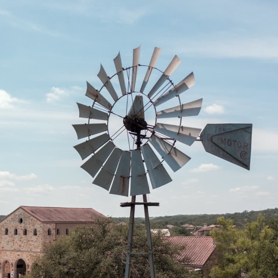A windmill sits on top of a hill in front of a building.