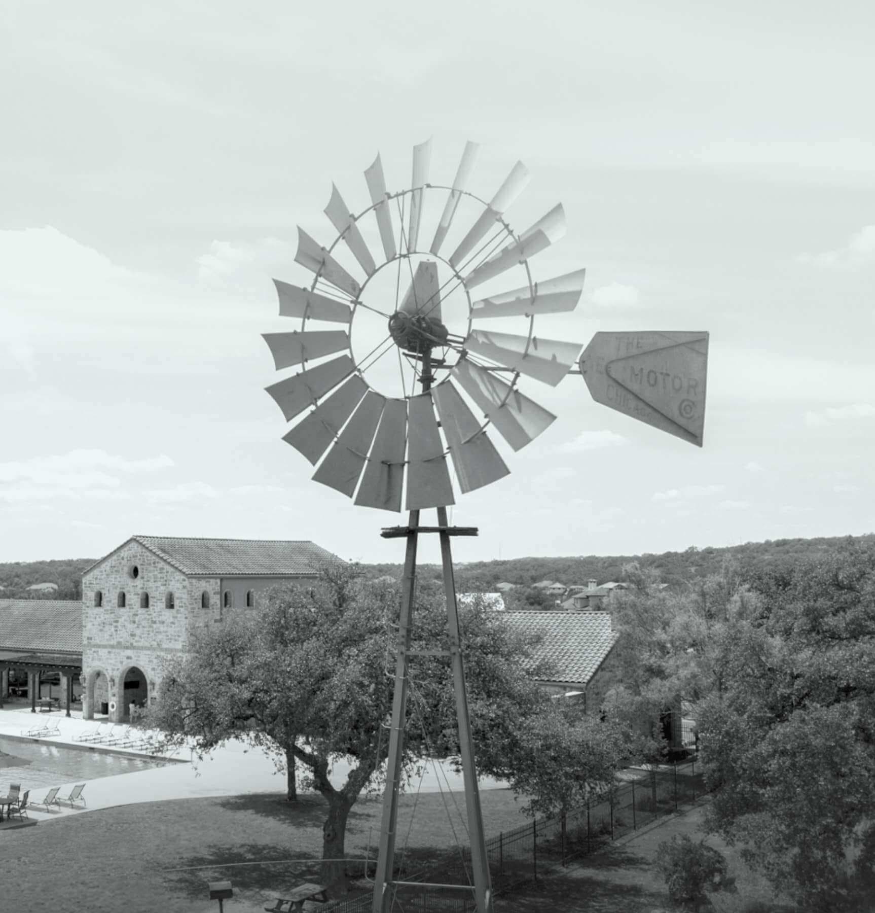 A black and white photo of a windmill in front of a pool.