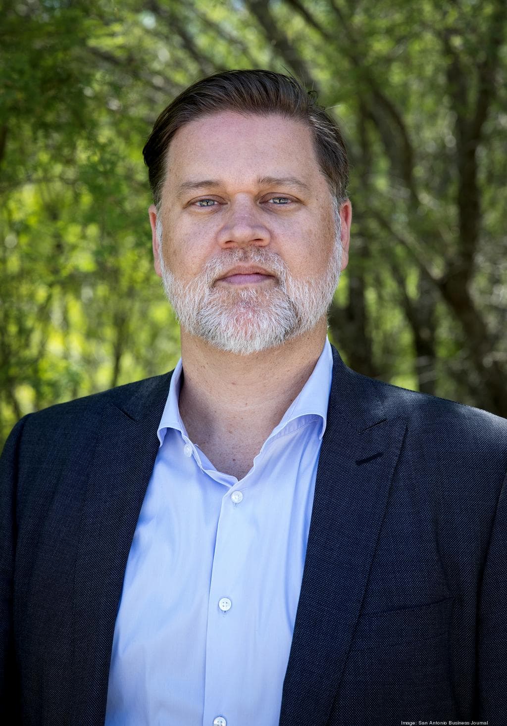 Thad Rutherford in a suit standing in front of trees.
