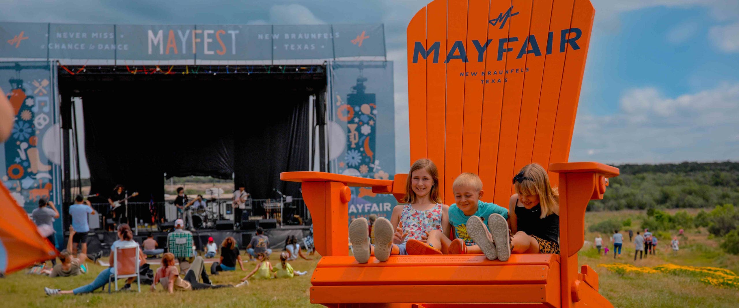 Young children sit in a fun oversized chair at Mayfest